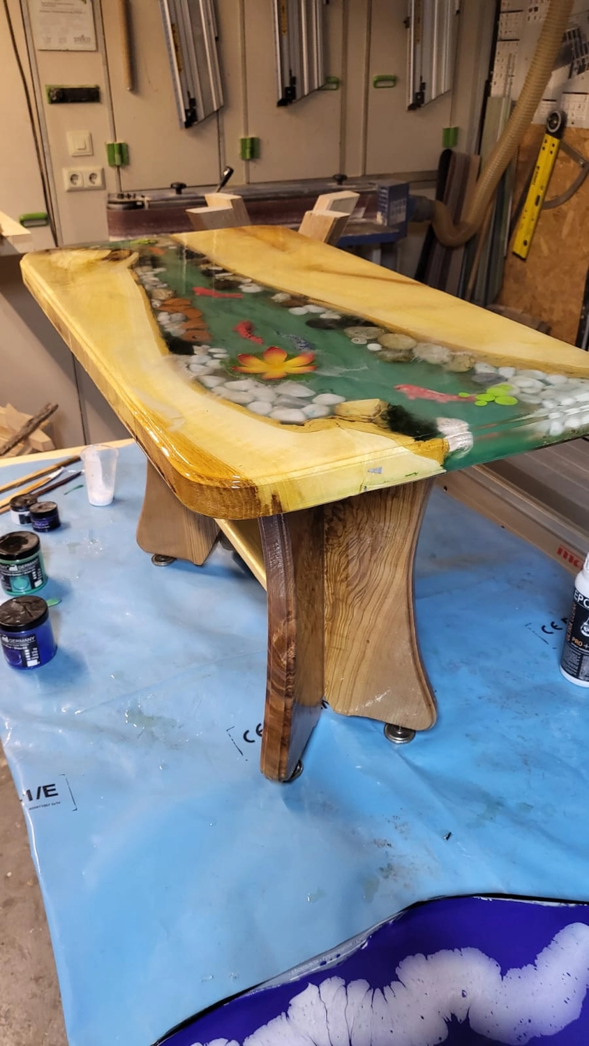 Dach,Wand und Holzkonstruktion - Handgefertigte Holzkunst - Ein Couchtisch aus naturbelassenem Holz mit einer aus grünem Epoxidharz gefertigten „Fluss“-Form und eingearbeiteten Dekorationselementen.