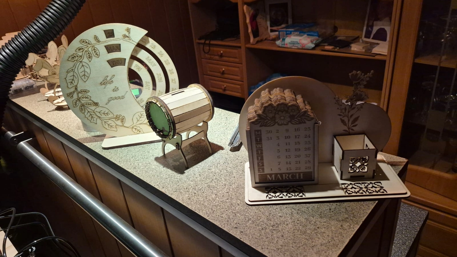 Dach,Wand und Holzkonstruktion - Handgefertigte Holzkunst - Eine Sammlung detailreicher 3D-Holzmodelle, darunter eine Miniaturtrommel und ein Tischkalender, auf einer Theke ausgestellt.