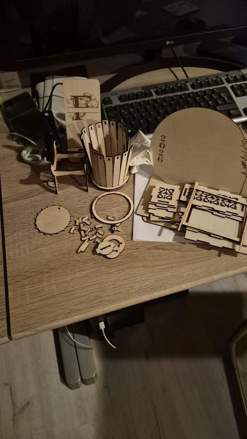 Dach,Wand und Holzkonstruktion - Handgefertigte Holzkunst - Verschiedene lasergeschnittene Holzteile, darunter ein kleiner Stiftehalter und flache Puzzleteile, auf einem Schreibtisch verstreut.