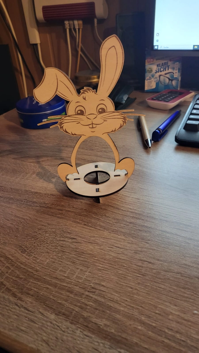 Dach,Wand und Holzkonstruktion - Handgefertigte Holzkunst - Eine lasergeschnittene Hasenfigur aus Holz auf einem hellbraunen Holzschreibtisch.