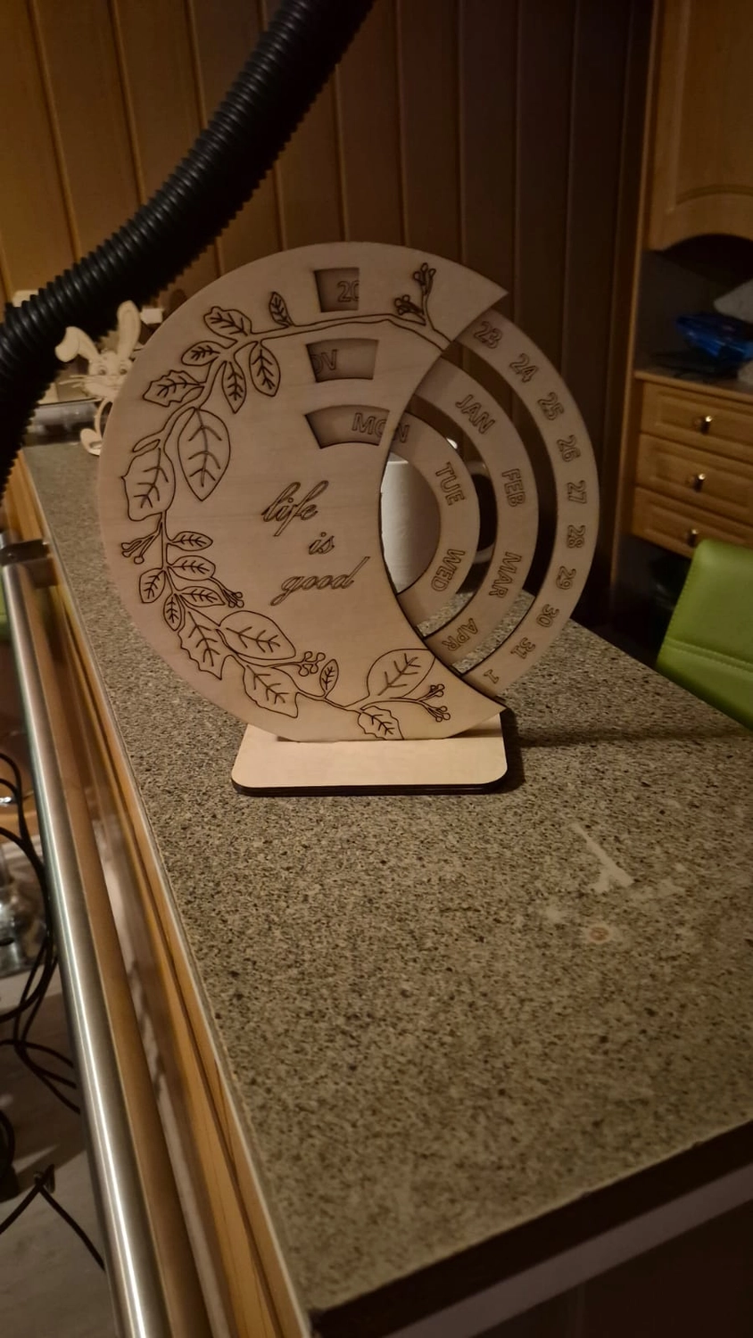 Dach,Wand und Holzkonstruktion - Handgefertigte Holzkunst - Ein lasergeschnittener, hölzerner Dauerkalender mit aufwendigen floralen Gravuren auf einer Arbeitsplatte.