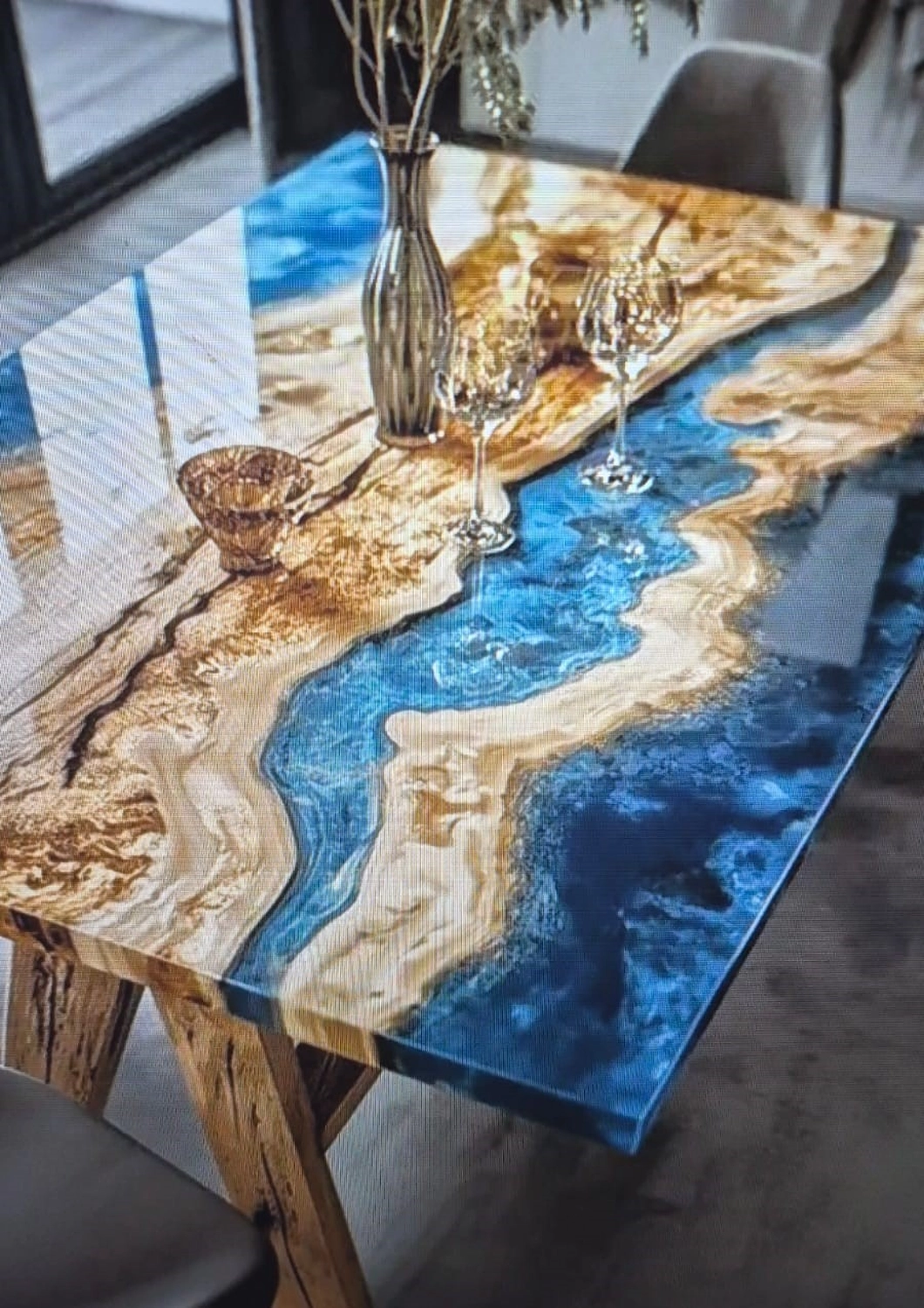 Dach,Wand und Holzkonstruktion - Handgefertigte Holzkunst - Nahaufnahme eines luxuriösen „Flusstisches“ aus naturbelassenen Holzbohlen, die durch einen geschwungenen Pfad aus leuchtend blauem Epoxidharz verbunden sind. Der Tisch hat eine hochglänzende Oberfläche, die das Umgebungslicht reflektiert.